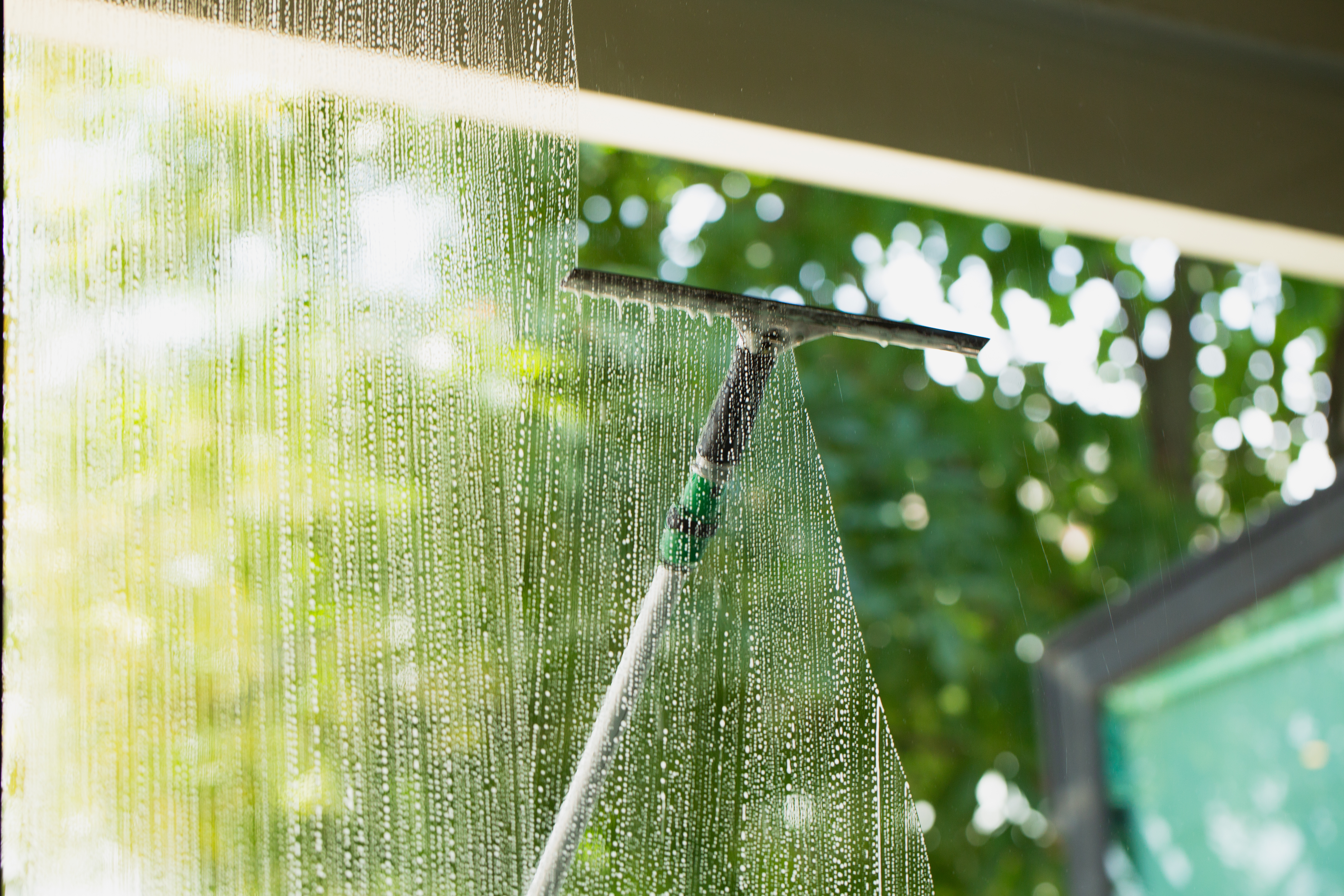 A professional window cleaner squeegeeing the soap off of a window. 