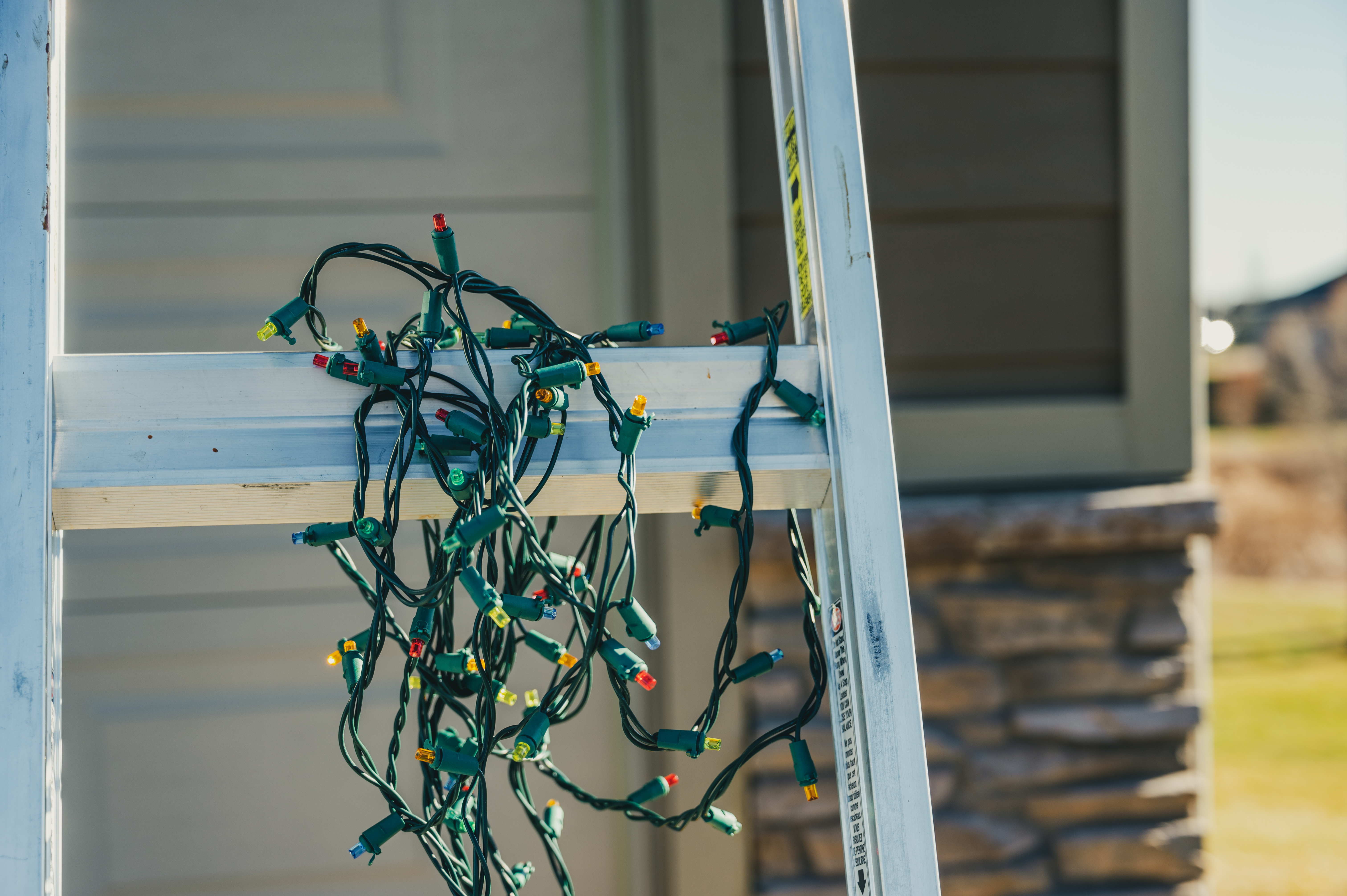 Holiday string lights sitting on a ladder rung. 