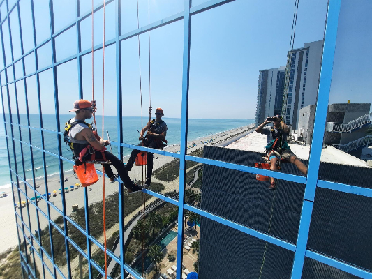 Two Window Ninjas team members cleaning the windows outside a high-rise commercial building.