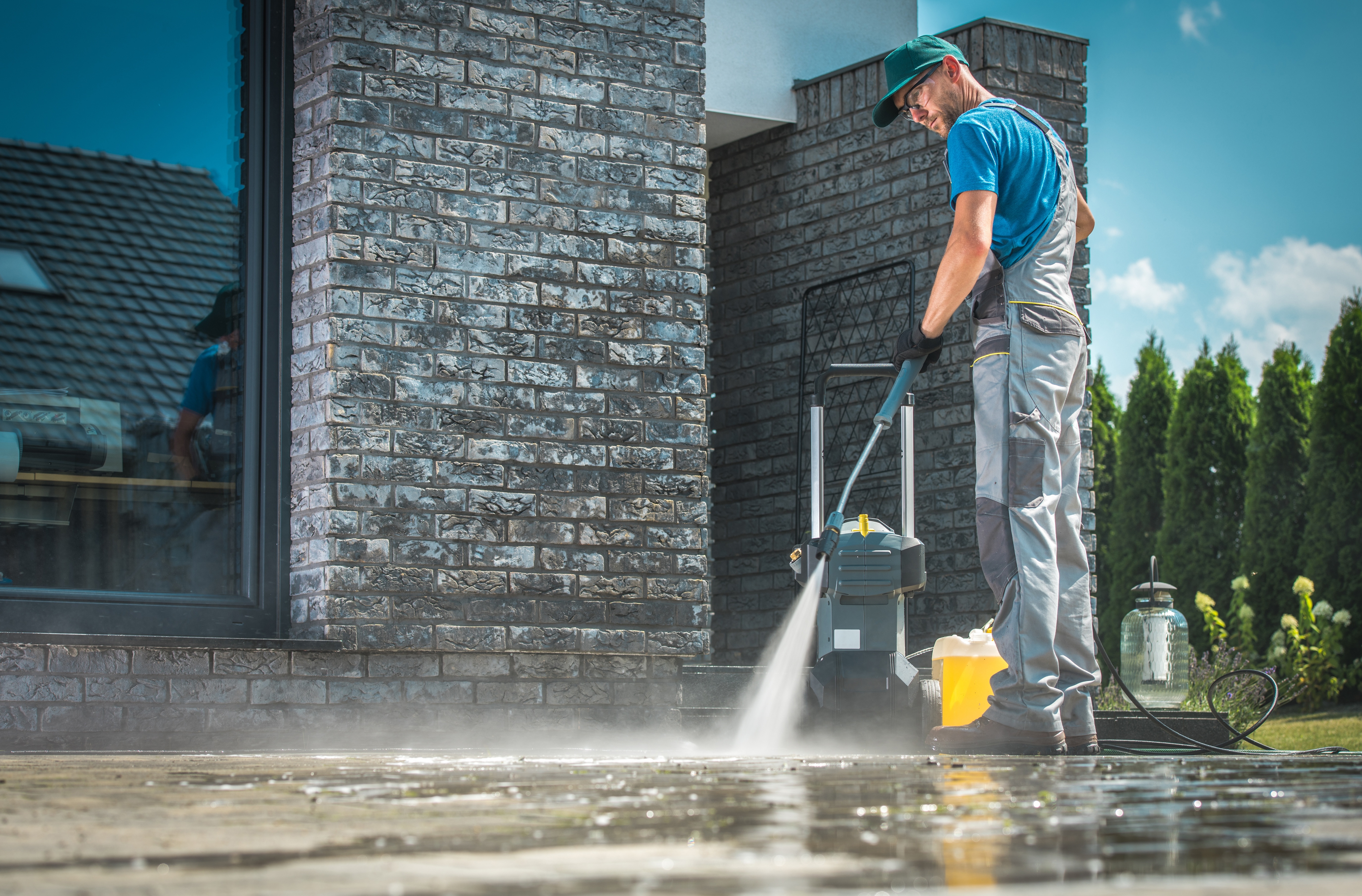 A Window Ninjas technician pressure washing the ground in front of a storefront.