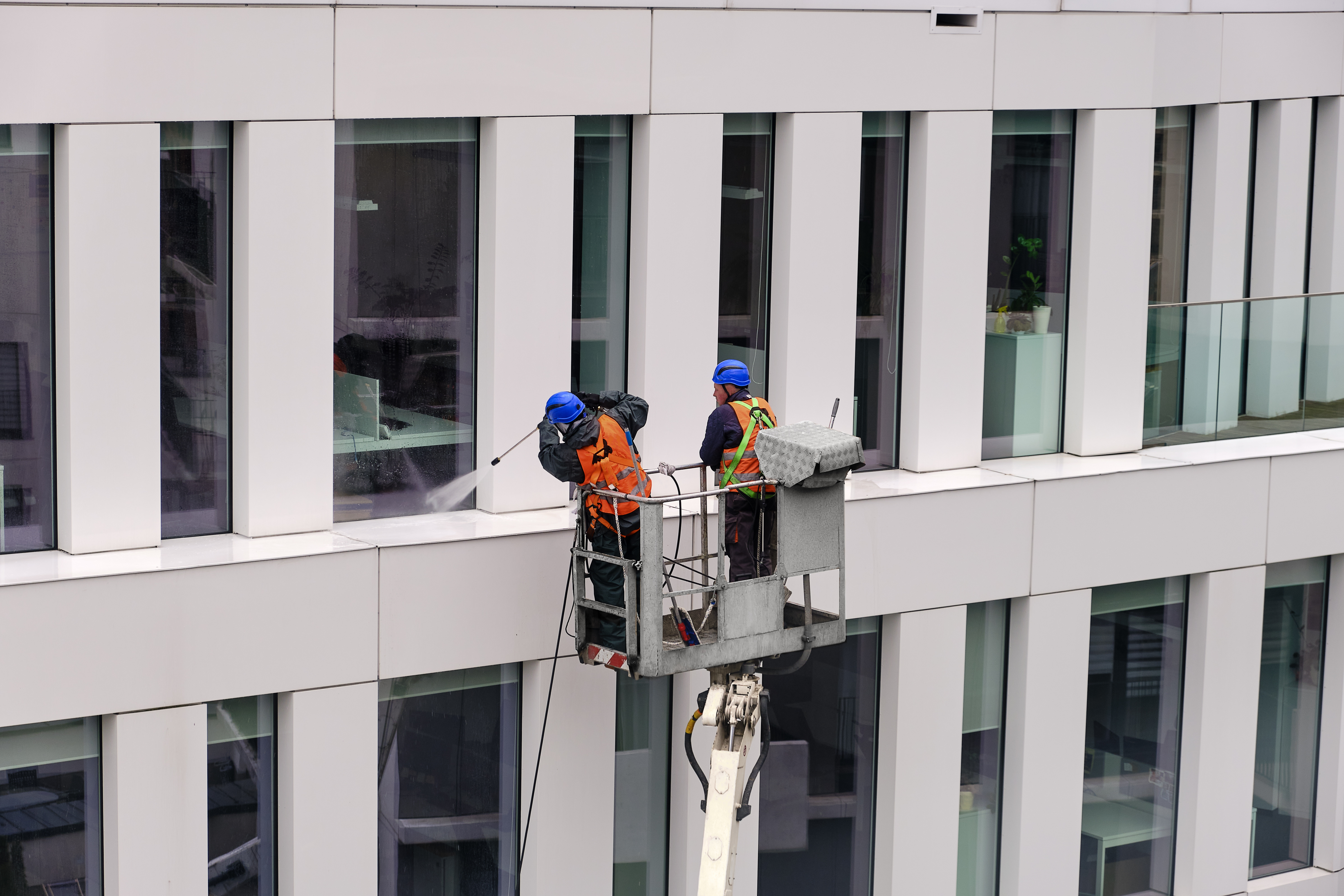 Two Window Ninjas technicians pressure washing the exterior of a commercial building.