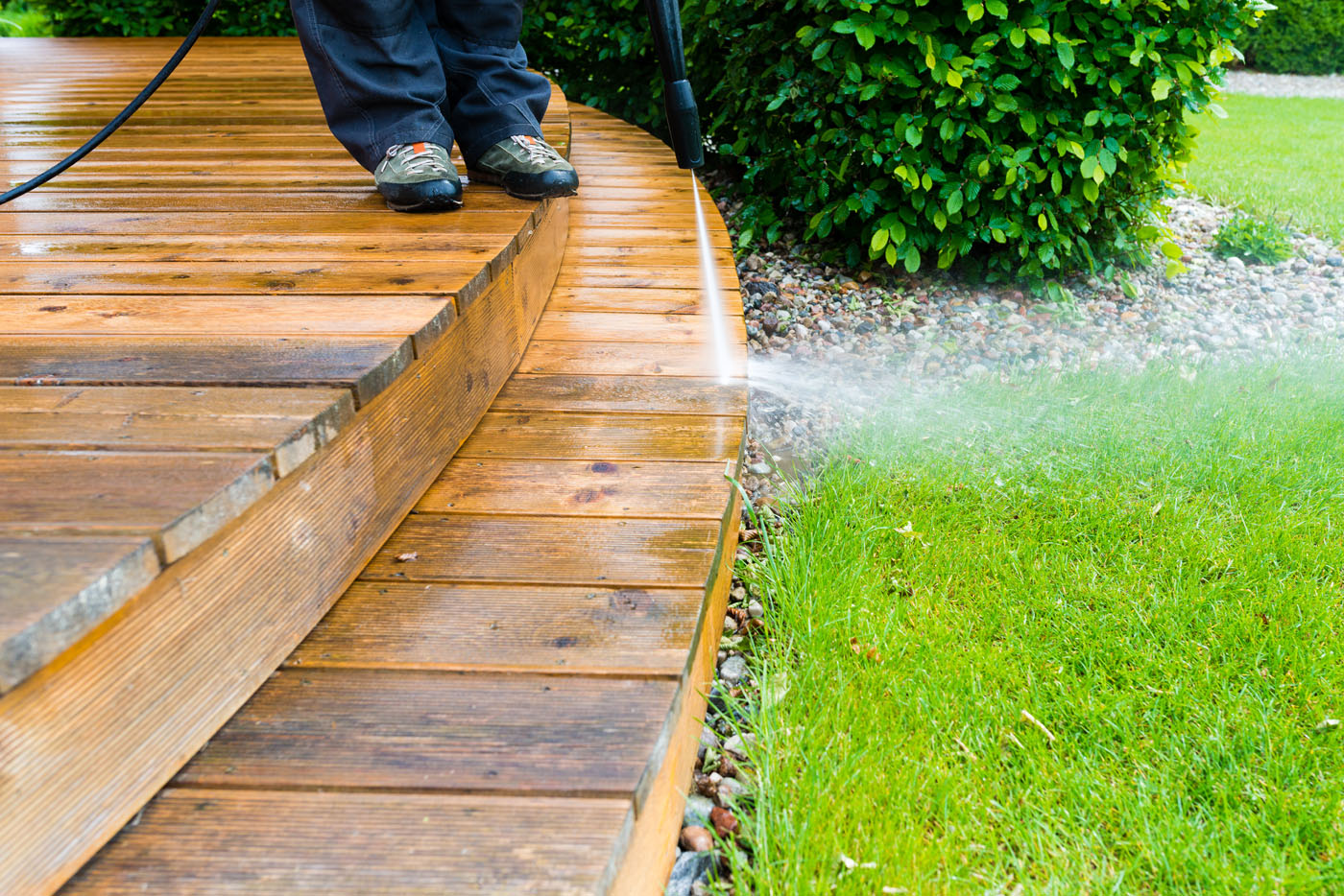 Someone cleaning a wooden surface / patio with power washing - discover the best exterior pressure washing with Window Ninjas.