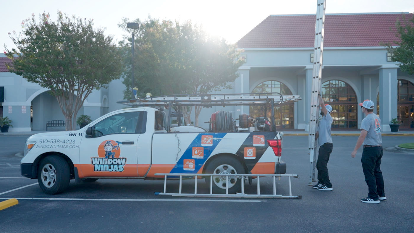 Two Window Ninjas team members taking a ladder off of a truck. 