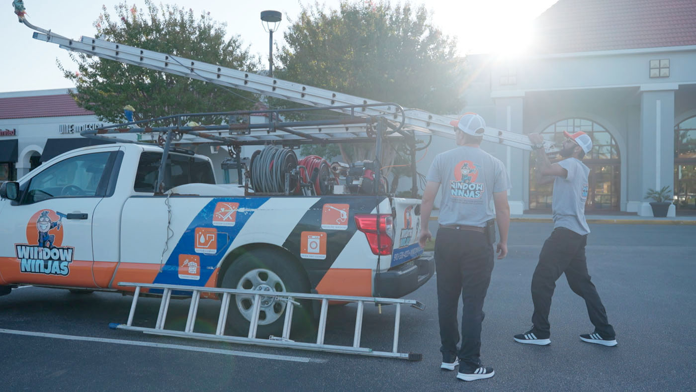 Two Window Ninjas team members removing a ladder from a brand truck. 