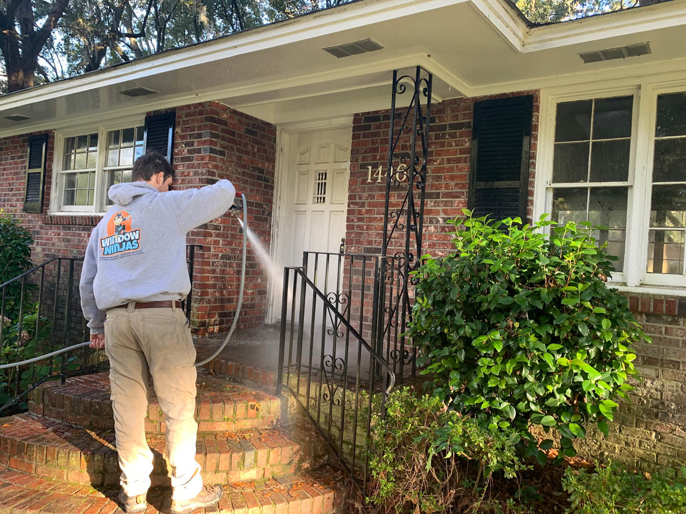 A Window Ninjas technician pressure washing a residential front porch.