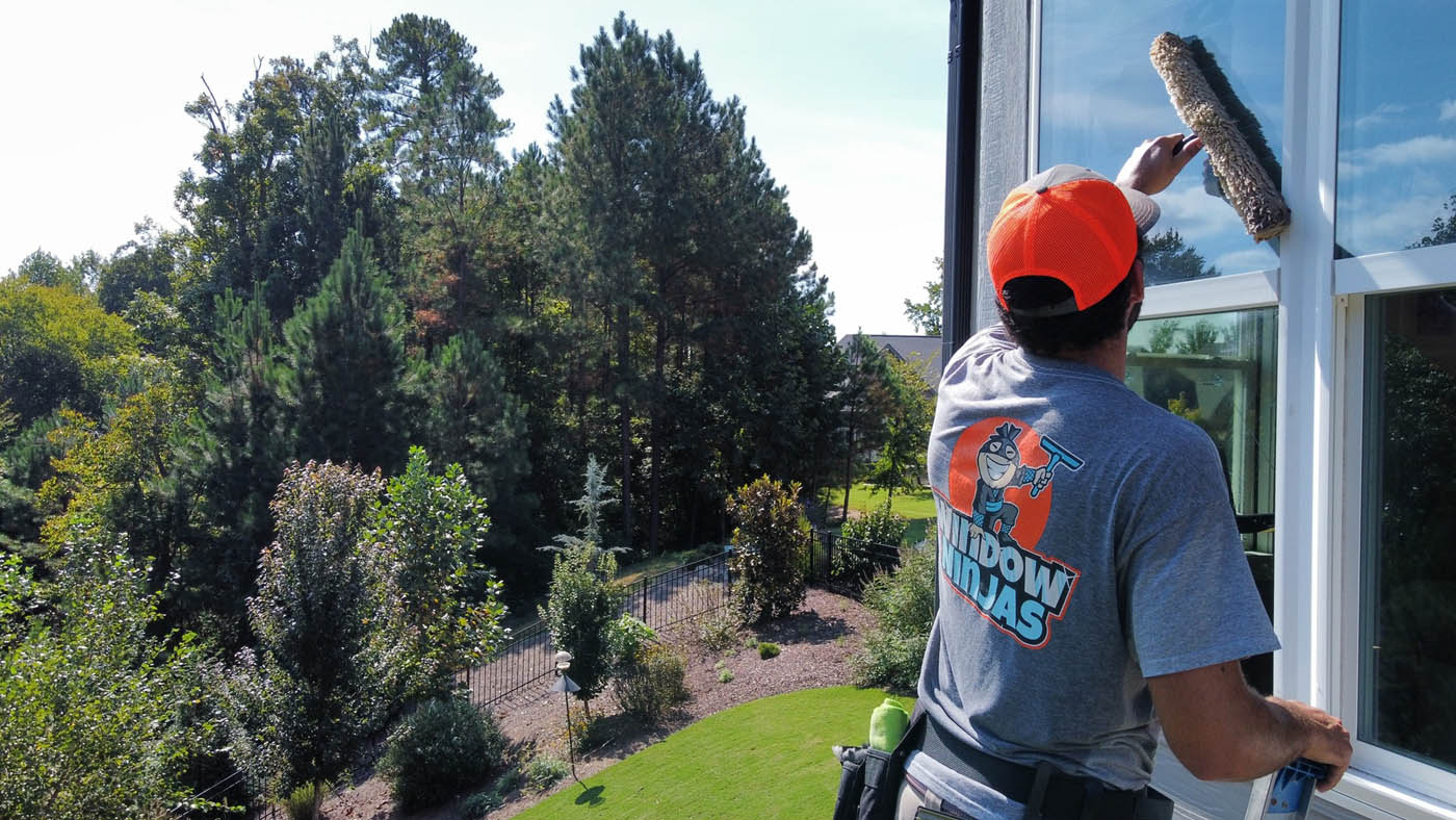 A Window Ninjas washing expert cleaning the outside windows for a tall residential home.