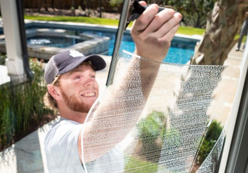 A person with a yellow glove using a squeegee to clean the soap off of a window.