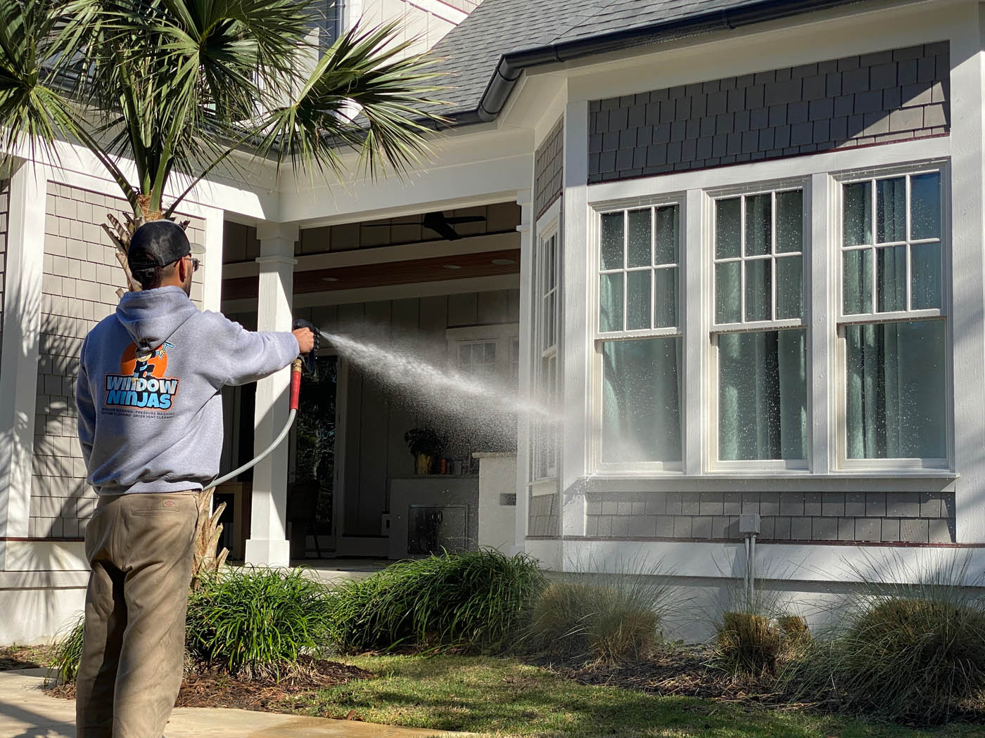 A Window Ninjas cleaning technician using a power washer to clean the surface of a home window.